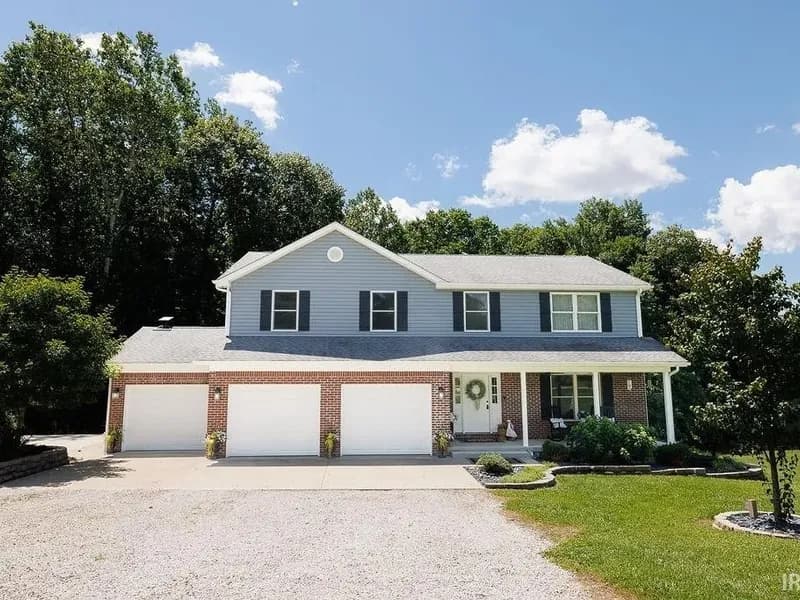 Front exterior of 1162 W Thornridge Way in Spencer, Indiana: a two-story brick home with a three car garage on a wooded lot.