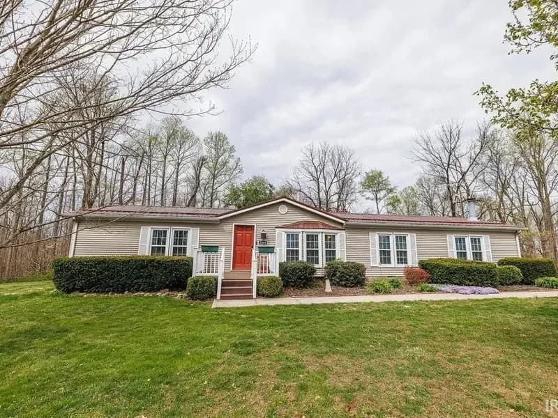 Front exterior of 2289 Dunn Rd in Freedom, Indiana: a ranch style home with a red front door and landscaped beds.