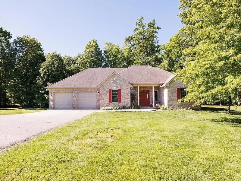 Front exterior of 2314 Parkview Dr in Spencer, Indiana: a brick ranch with red shutters at the end of a tree-lined driveway.