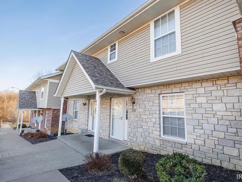 Front exterior of the townhome at 2407 S Woolery Mill Dr in Bloomington, Indiana, with stone and vinyl siding and a gabled entry porch.