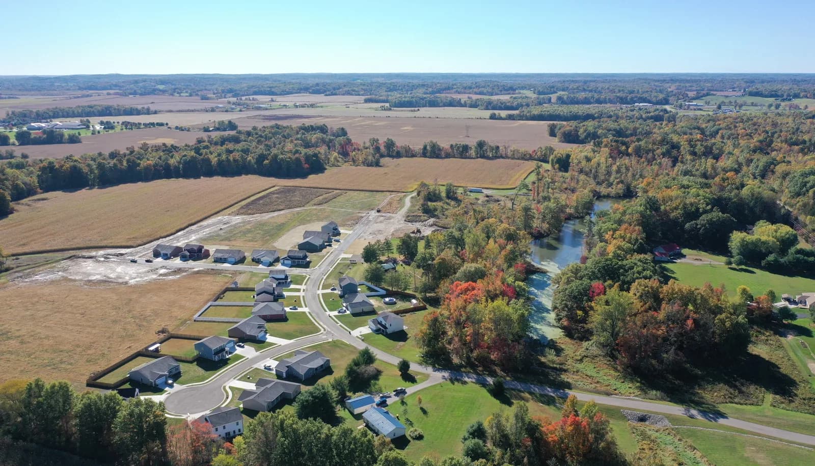 Autumn drone aerial over the Four Oaks neighborhood in Spencer, Indiana, with finished homes along curving streets and the creek beyond.