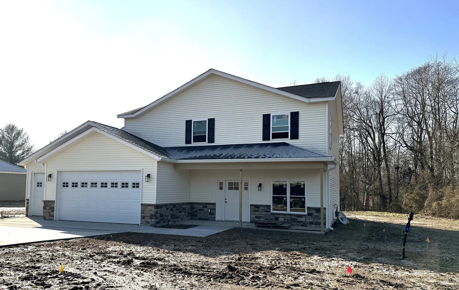 A newly built cream two-story home with stone accents at Four Oaks, photographed in winter.