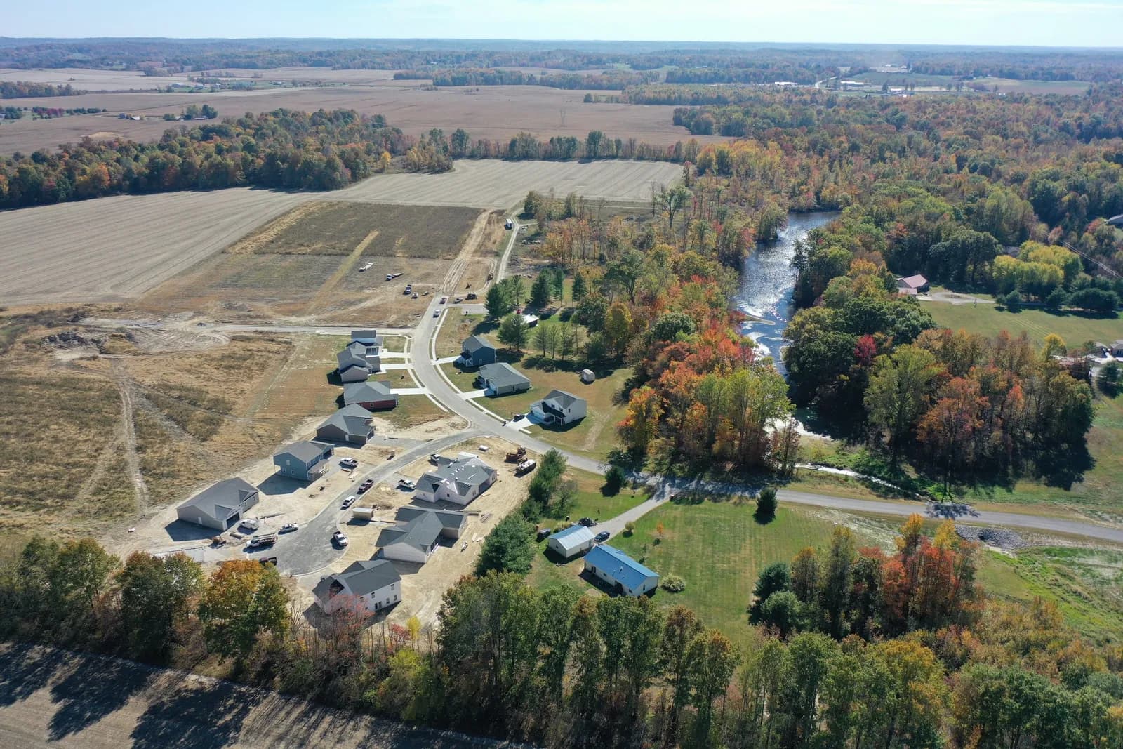 Autumn drone aerial of Four Oaks homes with the creek winding through the countryside beside them.