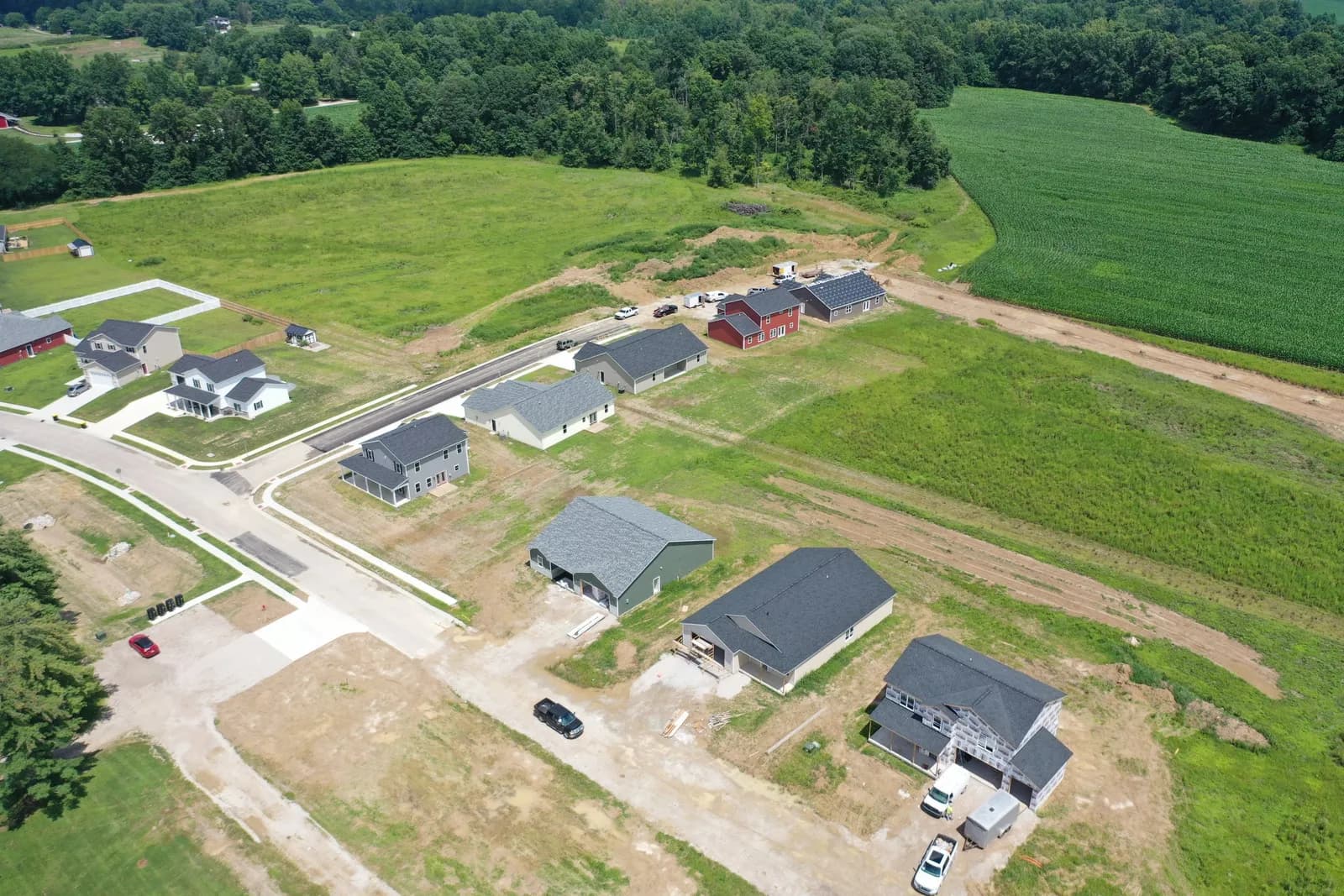 Summer drone aerial of new Four Oaks homes on a green hillside with open fields behind them.