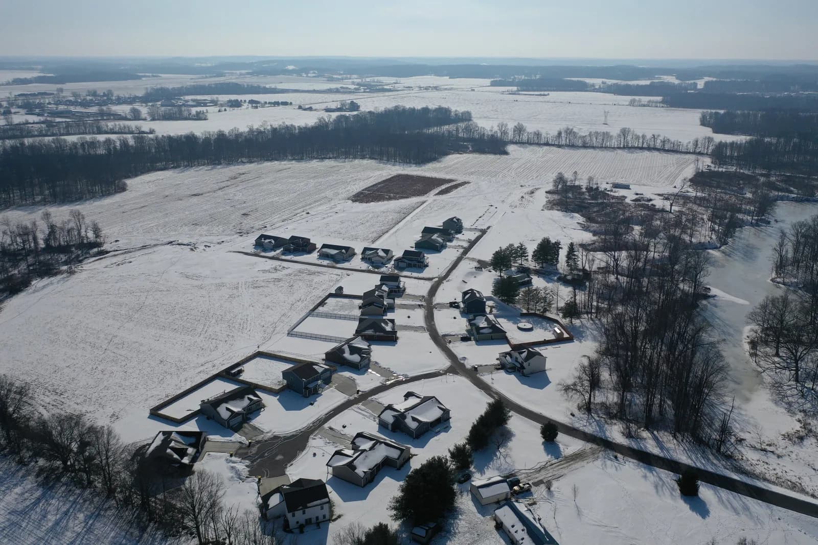 Winter drone aerial over the Four Oaks neighborhood with snow on the lots and finished homes along the curving streets.