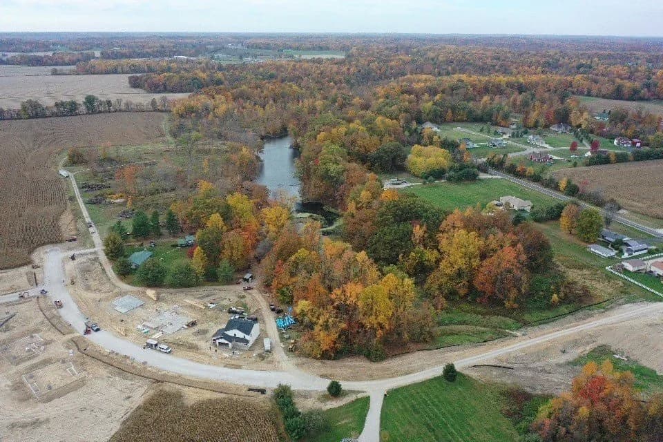 Autumn drone aerial over the Four Oaks pond, the tree line, and the first-phase lots.